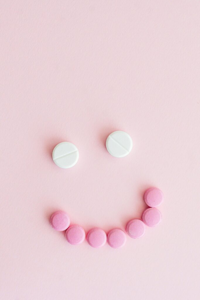 Smiley face made from pink and white tablets on a pastel pink background.